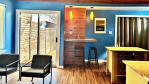 Une pièce avec un plafond en bois, un mur bleu, un plancher en bois, un coin bar et un espace salon avec des chaises.