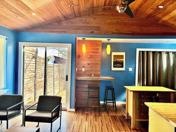 Una habitación con techo de madera, pared azul, suelo de madera, una zona de bar y un área de estar con sillas.