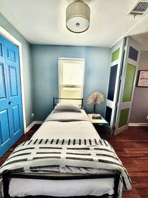 Un dormitorio con cama, mesita de noche, lámpara y puerta.