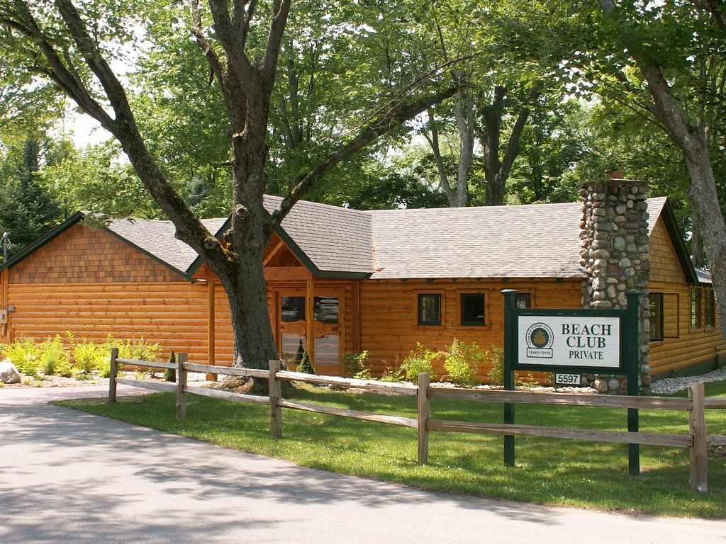 A wooden cabin with a stone chimney, surrounded by trees, labeled as a private beach club.
