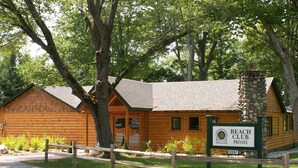 Une cabane en bois avec une cheminée en pierre, entourée d’arbres, et portant l’inscription « club de plage privé ».
