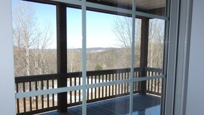 Une terrasse couverte avec une rambarde en verre, un plancher en bois et une vue sur une zone boisée.