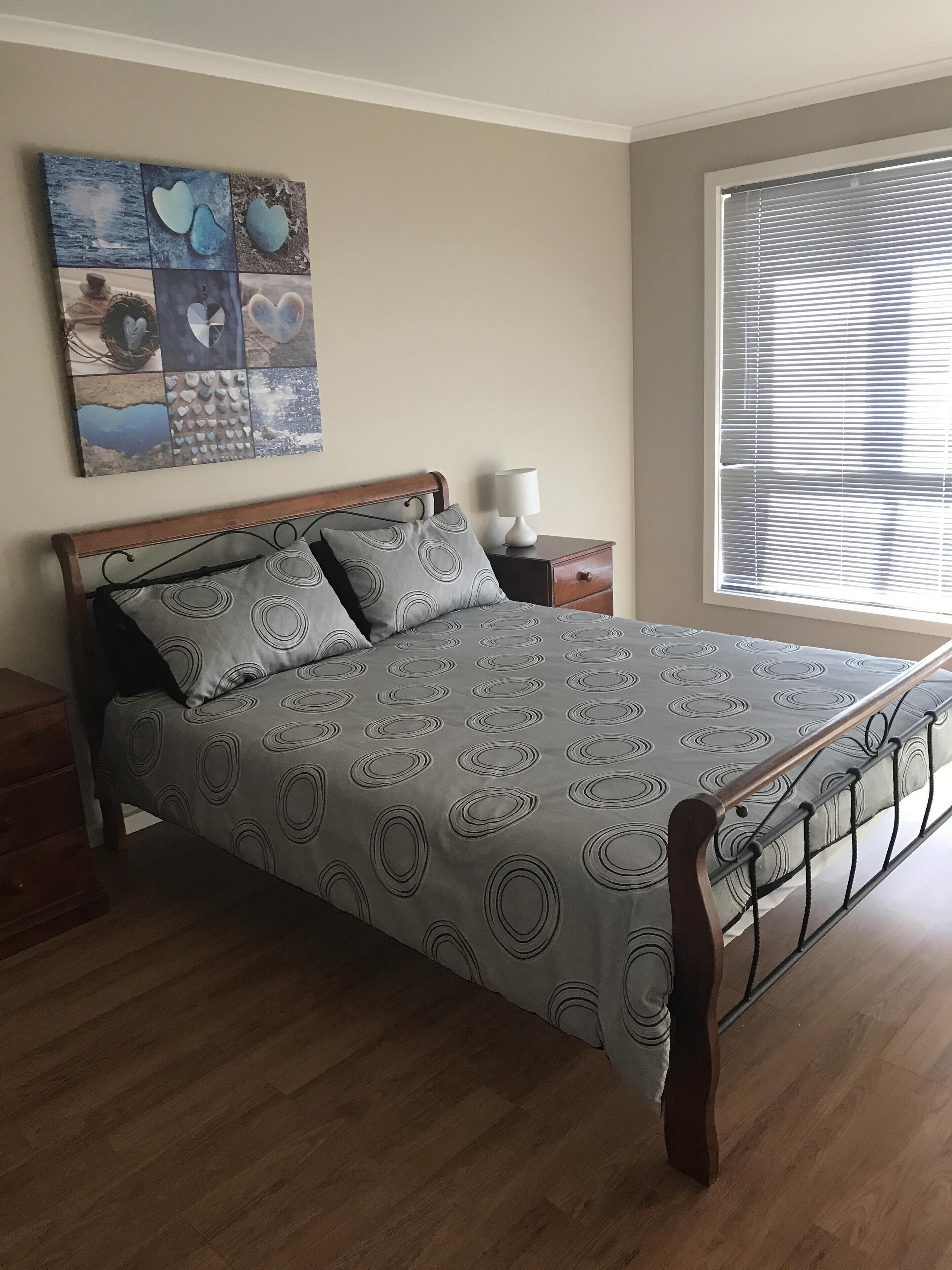 Una camera da letto con un letto in legno, biancheria grigia con motivi circolari, un comodino con una lampada e un quadro appeso sopra il letto.