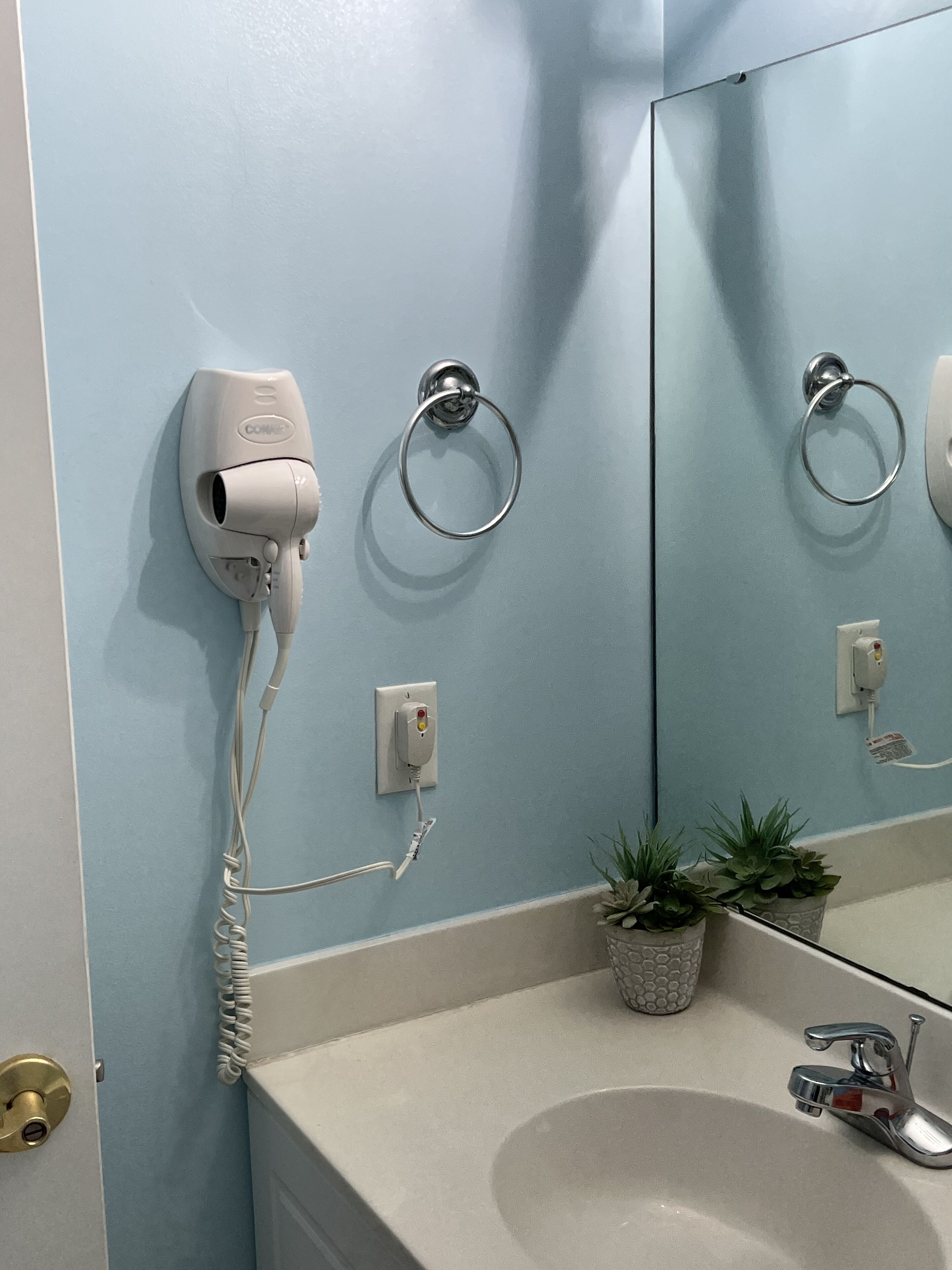 Een badkamer met een haardroger, handdoekhouders, een wastafel en een spiegel.