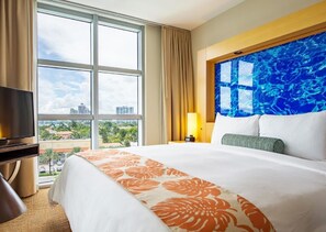 A hotel room with a large bed, a television, a window with a city view, and a decorative wall.