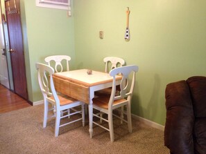 A dining area with a wooden table and white chairs, a brown couch, and a wall-mounted clock. - Escape to the Lake! (Port Clinton)