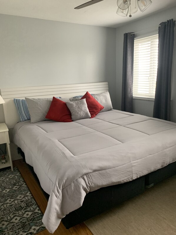 A neatly made bed with a white headboard, a patterned rug, and a window with curtains. - Escape to the Lake! (Port Clinton)