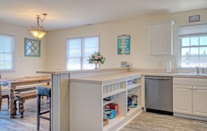 A kitchen with white cabinetry, a built-in dishwasher, and a dining area with a wooden table and chairs.