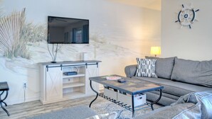 Ein Wohnzimmer mit Flachbildfernseher an der Wand, einer Couch, einem Couchtisch und einem Beistelltisch.