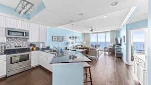 A spacious kitchen with white cabinets, a large island, and a view to the living area.