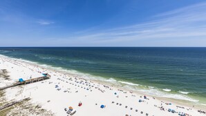 A beach with a long stretch of sand, a pier, and a building with a blue roof.