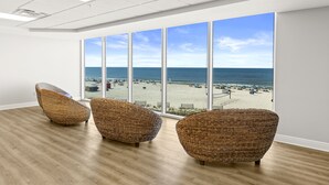 A room with large windows overlooking a beach, featuring three wicker chairs and wooden flooring.