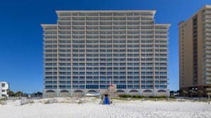 A large hotel with multiple floors and balconies, situated on a sandy beach with clear skies.