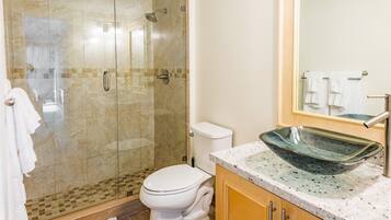 A bathroom with a glass-enclosed shower, a toilet, a sink with a glass bowl, and a mirror above the sink.
