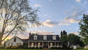 Une maison à deux étages avec un porche à l’avant, une cheminée et une pelouse bien entretenue.