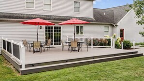 Une maison dotée d’un patio couvert, agrémenté de deux parasols rouges, d’une clôture blanche et d’une pelouse verdoyante.