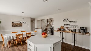 Une cuisine moderne dotée d’un îlot central, de chaises en bois, d’une table à manger et d’un escalier menant à un niveau supérieur.