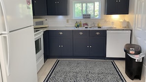 Una cucina moderna con pensili scuri, un frigorifero bianco, un forno a microonde e una lavastoviglie. Una finestra offre vista su una zona verde.