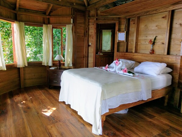 A wooden cabin bedroom with a bed, nightstand, and window with curtains.