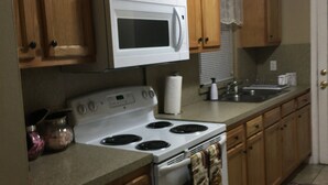 Una cocina con armarios de madera, un microondas blanco, una estufa y un lavamanos.