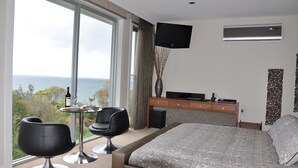 Una habitación de hotel con cama, televisor, escritorio con silla y vista al océano.