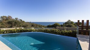 Una piscina azul clara con vista al océano y colinas.