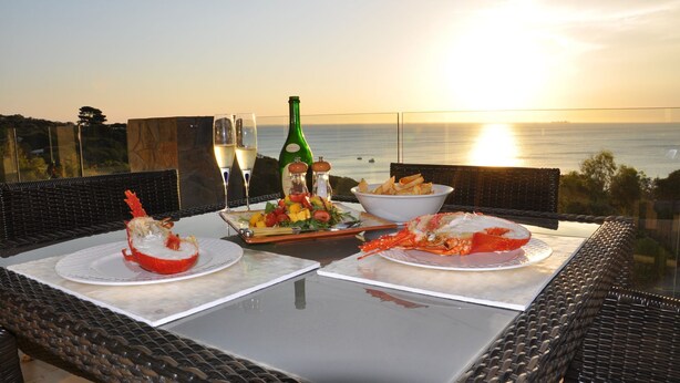Una mesa servida para una comida con mariscos, una botella de champán Brut y vistas al mar.