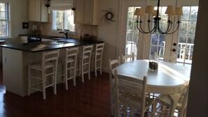Una cocina con una isla central, sillas blancas, una mesa de comedor y una araña.