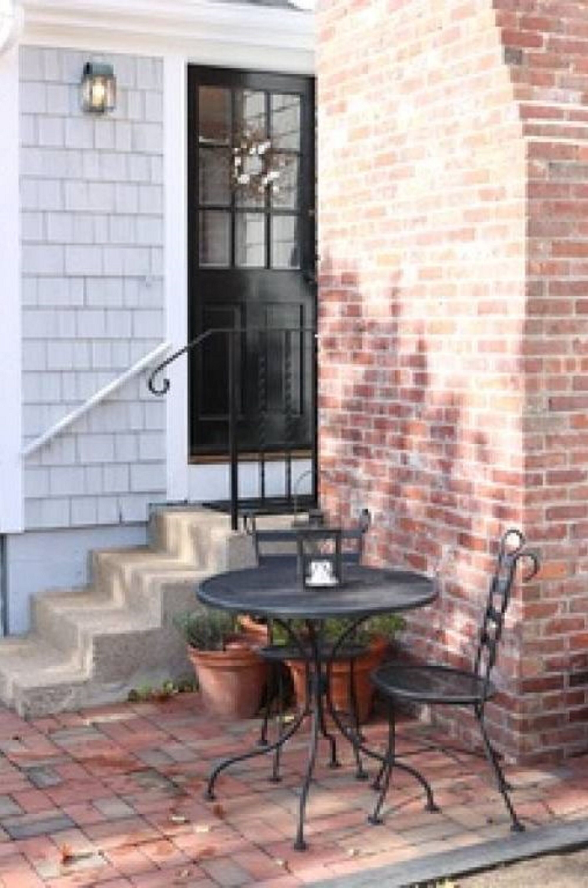 A patio with a round table and two chairs, a brick wall, and a black door with a window.