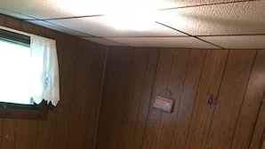 A compact room with two beds, wooden walls, a small window with a curtain, and a tiled floor. - Piedmont lake hunting and fishing cabin (Freeport)
