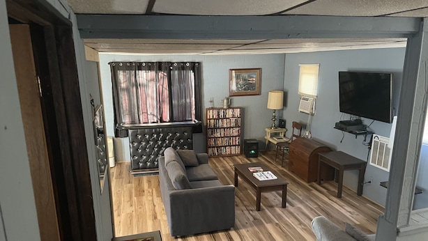 A living room with a sofa, a coffee table, a bookshelf, a television, and a window with curtains. - Piedmont lake hunting and fishing cabin (Freeport)