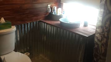 A bathroom with wooden walls, a white toilet, a sink with a mirror, and a window with a curtain.