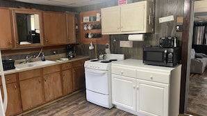 A compact kitchen with wooden cabinets, a stove, a microwave, and a sink. - Piedmont lake hunting and fishing cabin (Freeport)