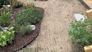 Un sendero en el jardín con acolchado, plantas y una terraza de madera.