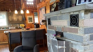 Interior acogedor de una cabaña con chimenea de piedra, vigas de madera en el techo y una zona de comedor con una mesa grande y sillas.