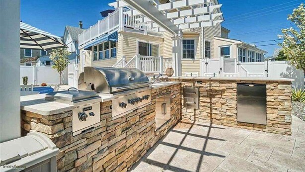 Un'area cucina esterna con parete in pietra, barbecue e struttura a pergola.
