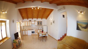 Un'ampia zona giorno con soffitto in legno, un tavolo da pranzo con sedie, un divano e una cucina sullo sfondo.