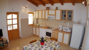 Una cucina con mobili in legno, zoccolo di piastrelle, forno a microonde e tavolo da pranzo con sedie.