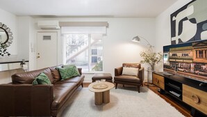 Un salon moderne avec un canapé en cuir marron, une table basse ronde, un fauteuil marron et un téléviseur posé sur un meuble en bois.