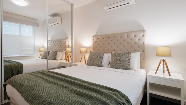 Une chambre d’hôtel avec un grand lit, un miroir, deux tables de chevet avec des lampes et un appareil de climatisation fixé au mur.