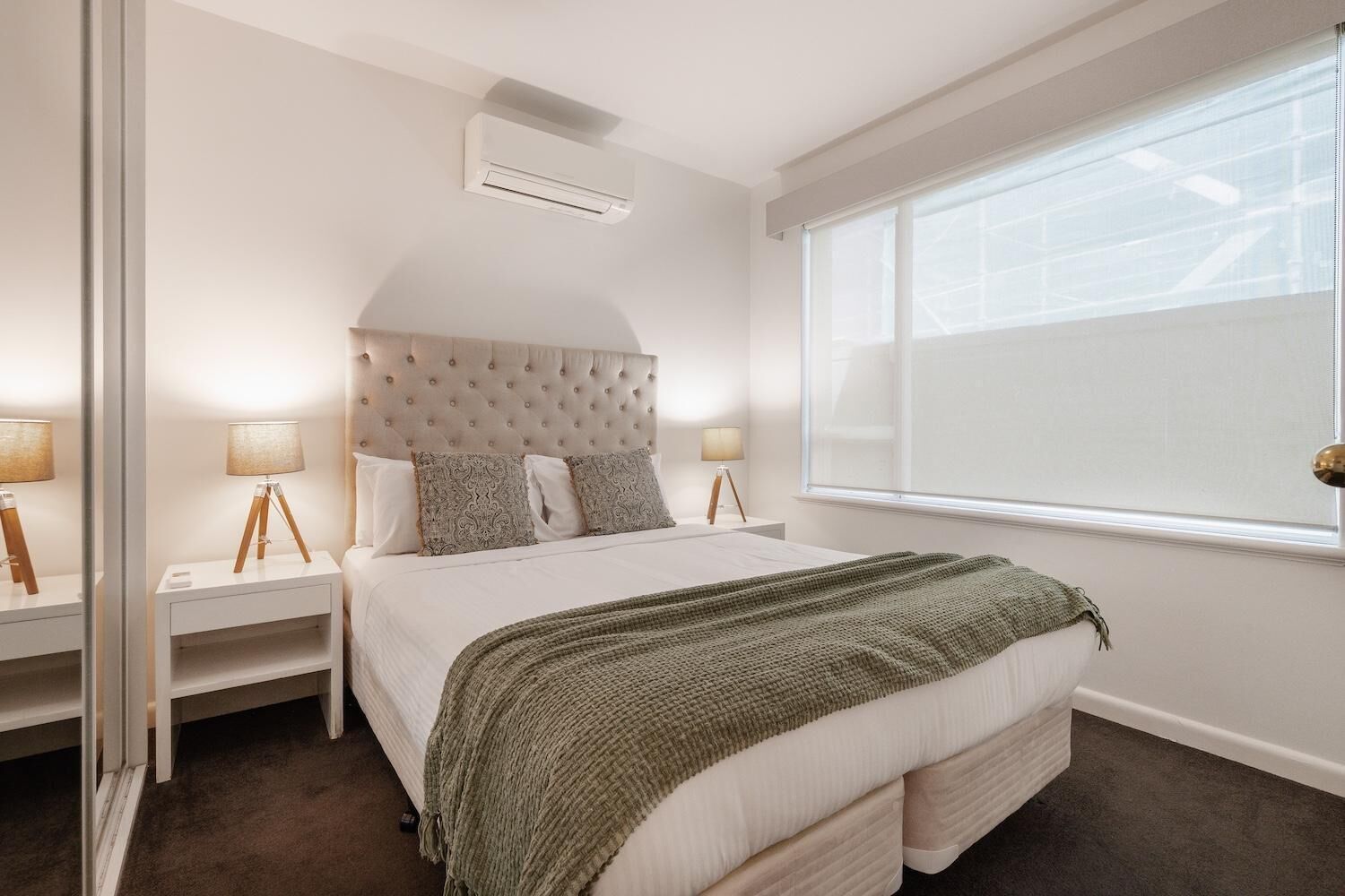 Een slaapkamer met een groot bed, twee nachtkastjes met lampen, een raam met jaloezieën en een airconditioning.