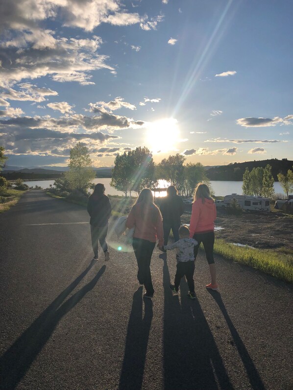 Une famille se promène sur un chemin pavé, avec un lac et des arbres en arrière-plan.