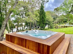 A hot tub in a wooden structure surrounded by trees and a grassy area.