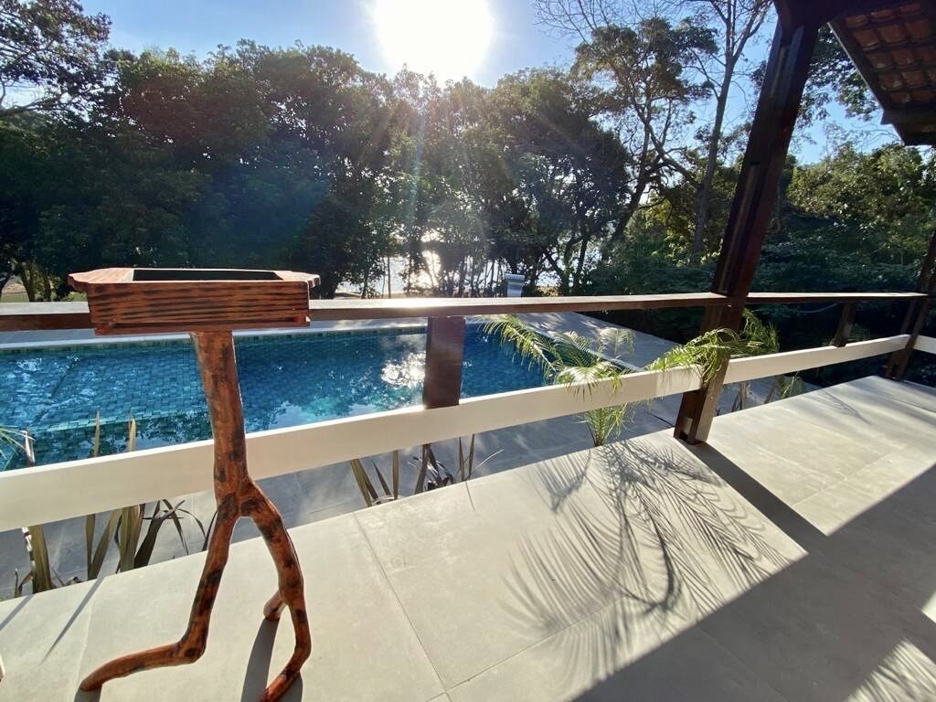 A poolside area with a wooden bench and a table, surrounded by a white railing and palm trees.