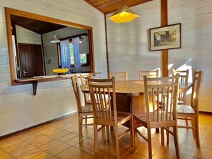A dining area with a wooden table and chairs, a hanging pendant light, and a framed picture on the wall.