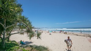 Ein Strand mit Palmen, badenden Personen und blauem Himmel.