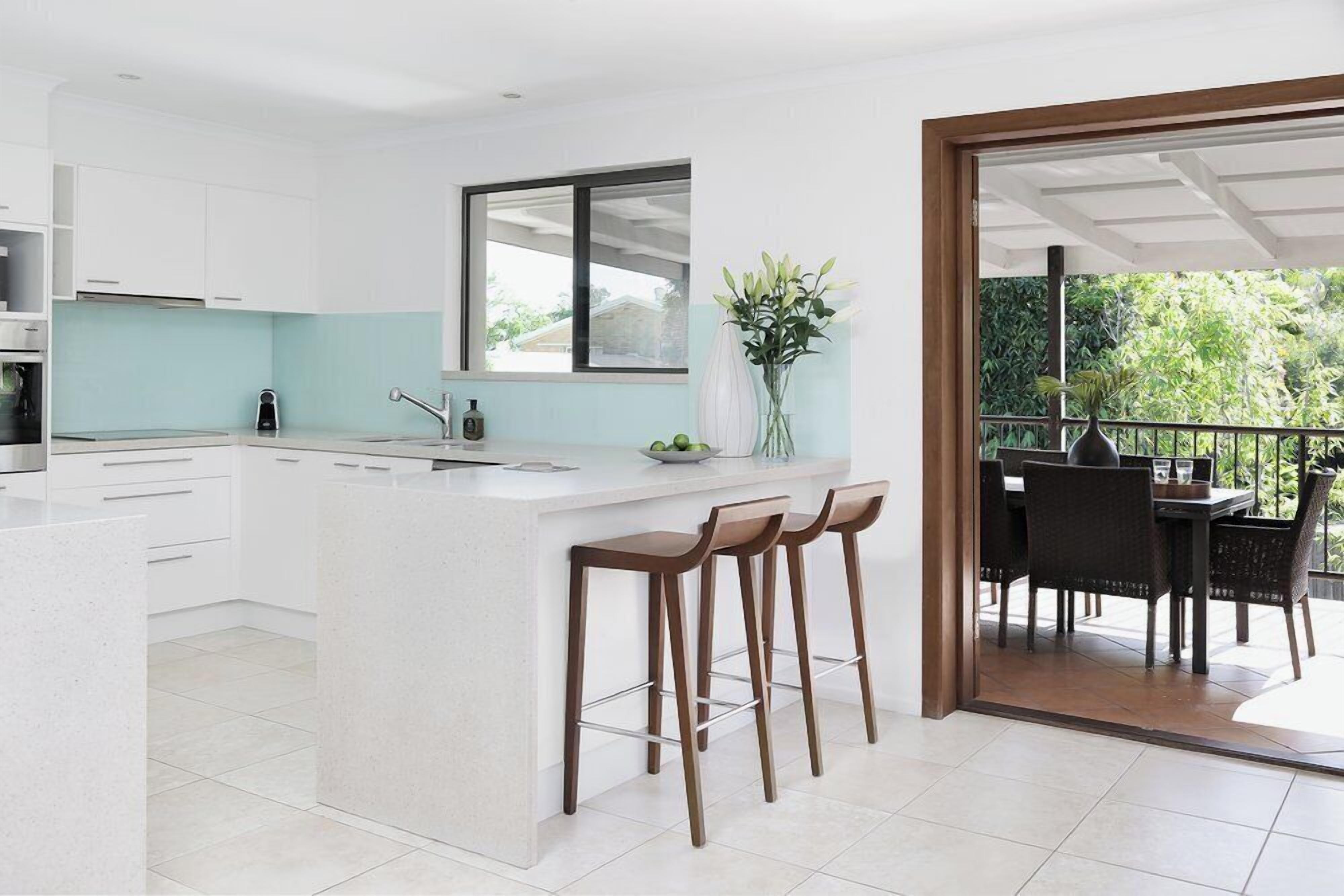 A modern kitchen with white cabinetry, a large island with stools, and a view of an outdoor patio with dining furniture.