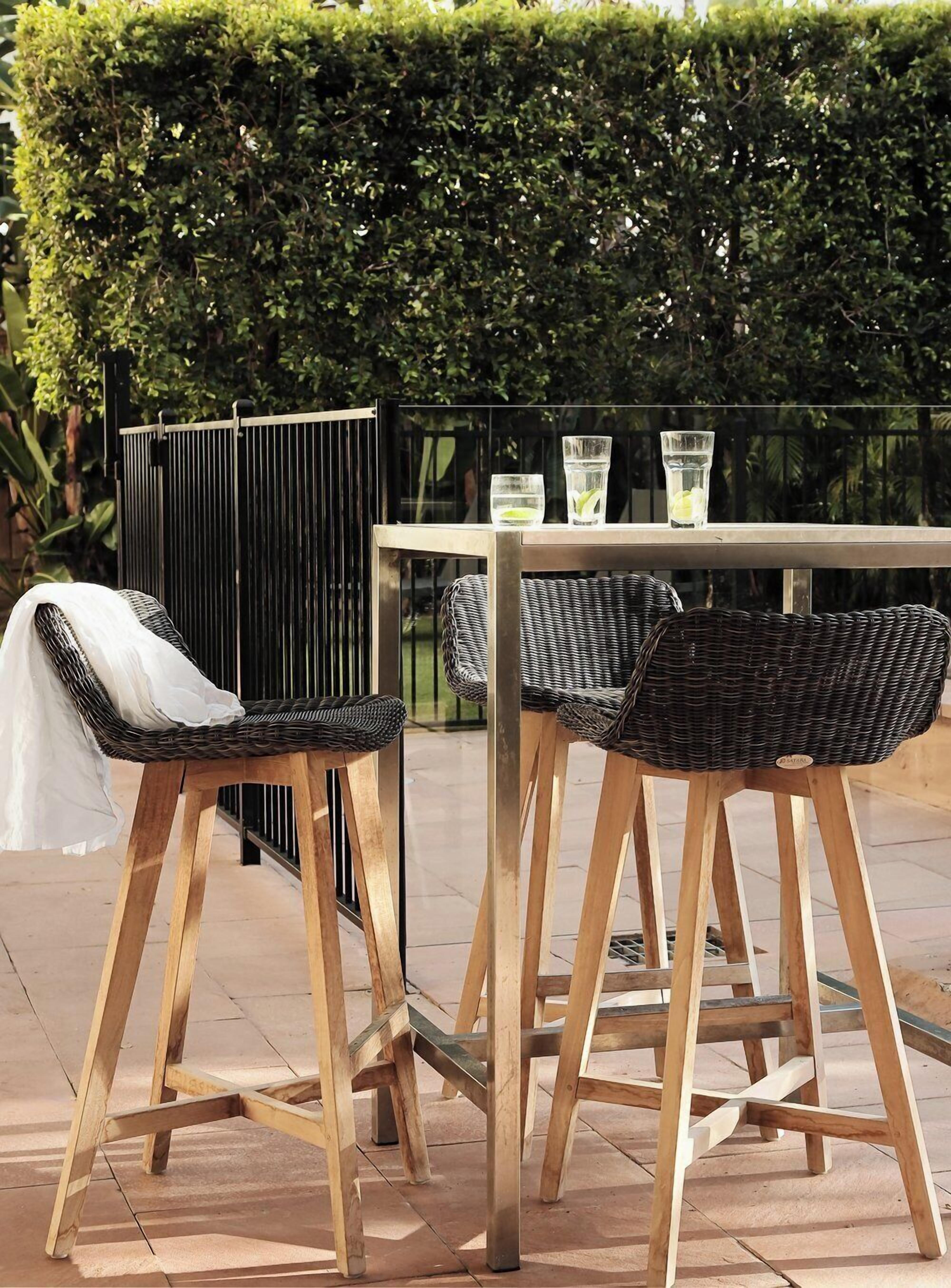 An outdoor seating area with two wicker chairs and a table, surrounded by a metal fence and a hedge.