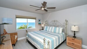 A bedroom with a bed, a nightstand, a chair, a window with a view of the ocean, and a ceiling fan. - Beachfront Condo - 3 BR- Heated Pool - Free Boat Docks – Upscale – Siesta Key (Siesta Key)