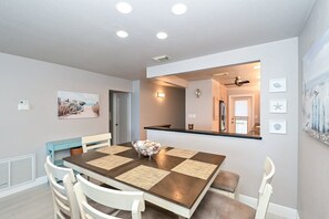 A dining area with a wooden table, white chairs, and a central island with a bowl of fruit. - Beachfront Condo - 3 BR- Heated Pool - Free Boat Docks – Upscale – Siesta Key (Siesta Key)